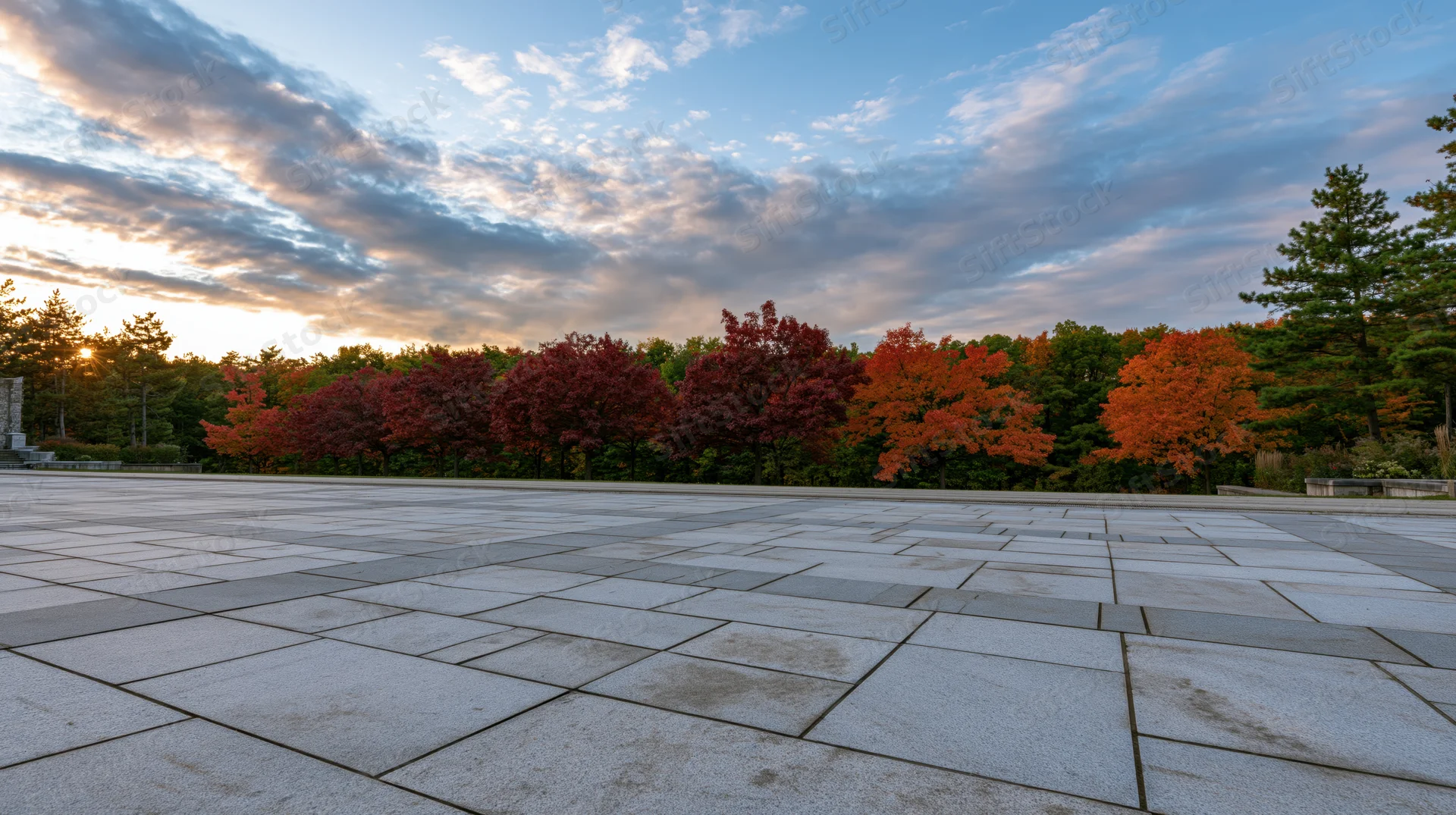 Wide granite tile plaza stretching to horizon with autumn trees and sunset sky