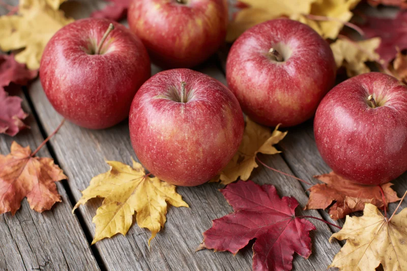 Red apples arranged on a weathered wooden surface with autumn leaves scattered around