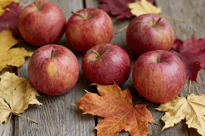 Red apples arranged on a weathered wooden surface with autumn leaves