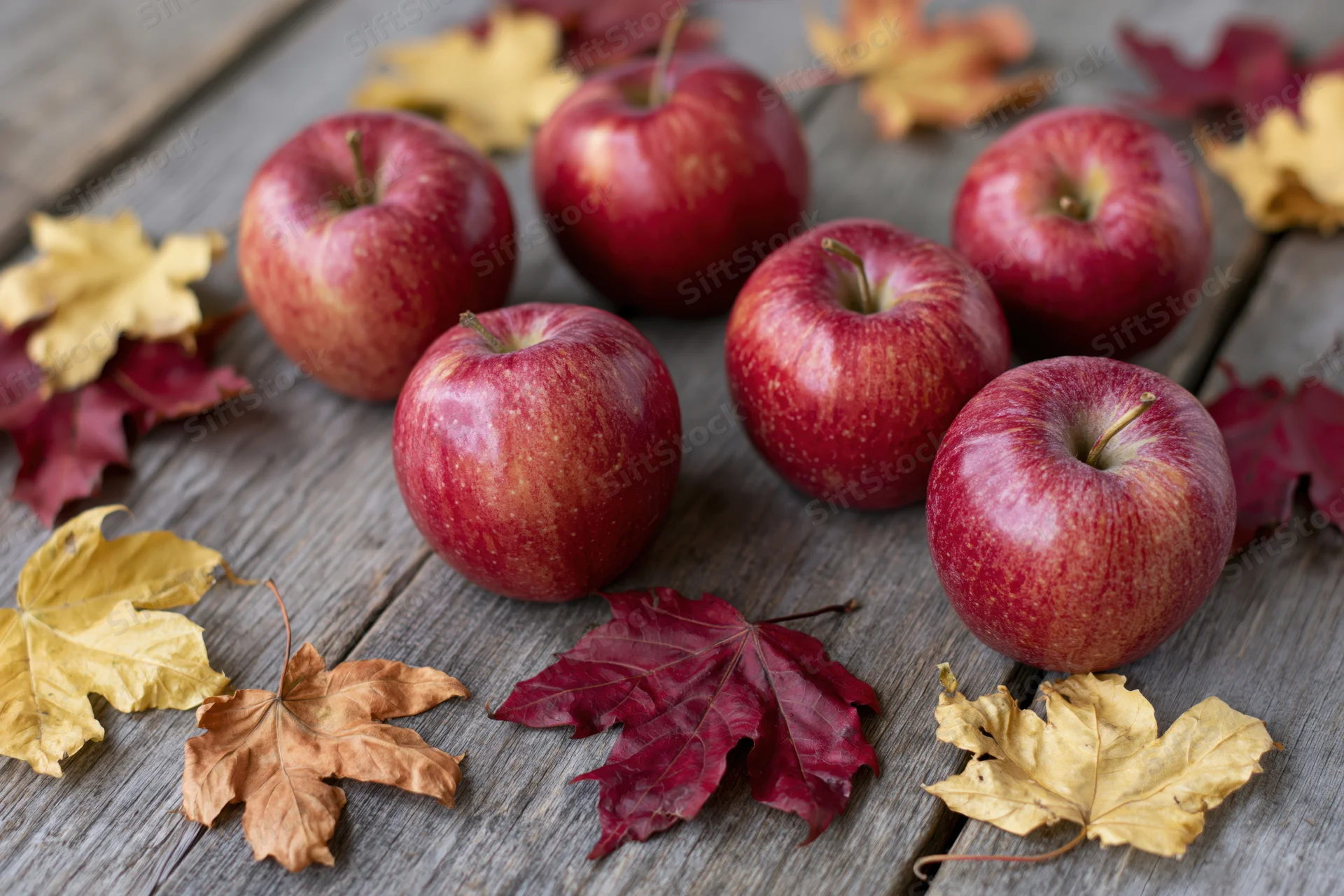 Red apples arranged with autumn leaves on a weathered wooden surface