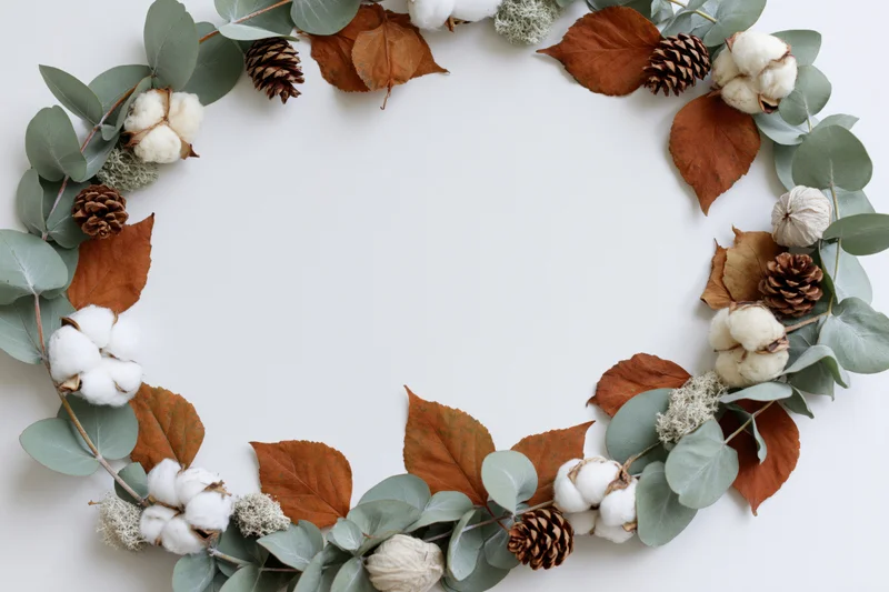 Circular wreath made of eucalyptus leaves, dried cotton bolls, pinecones and autumn leaves on white background