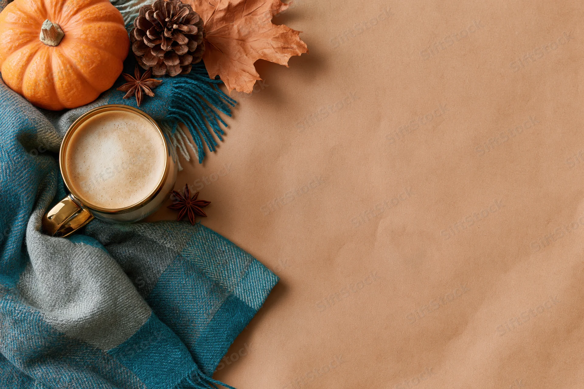 Latte in a gold glass mug with a plaid scarf and autumn decorations on a brown surface