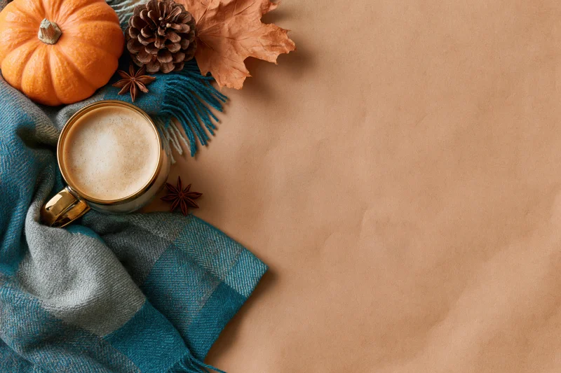 Latte in a gold glass mug with a plaid scarf and autumn decorations on a brown surface