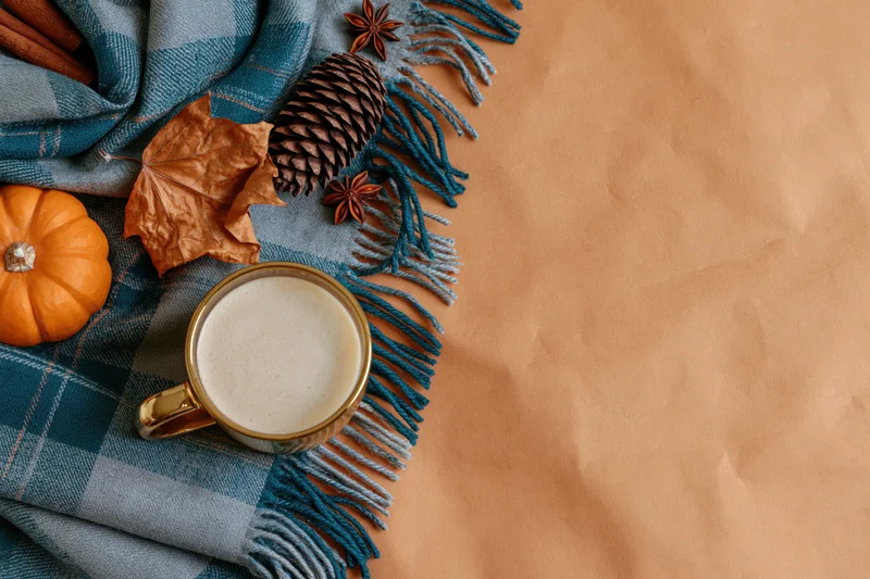 Latte in a gold glass mug on a plaid scarf with autumn decorations arranged on a brown paper surface