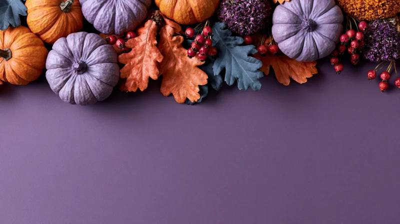 Autumn decorations including pumpkins, leaves and berries arranged along the top of a purple surface with copyspace below