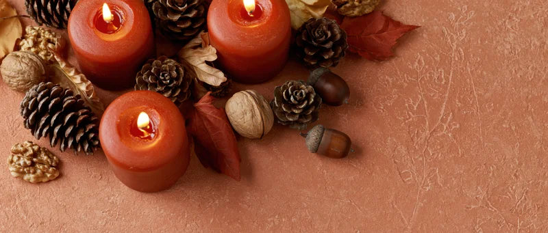 Lit red-orange candles with pinecones, acorns and autumn leaves arranged on textured surface