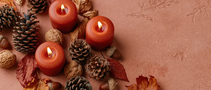 Lit red-orange candles arranged with pinecones, leaves and nuts on a textured terracotta surface
