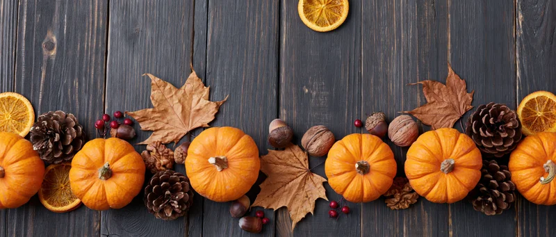 Small orange pumpkins arranged with autumn leaves, pinecones and dried oranges on dark wooden table