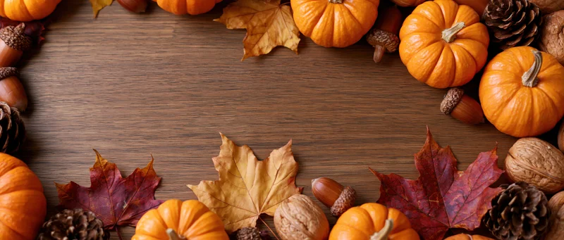 Small orange pumpkins and dried maple leaves arranged in a border on a wooden table with copyspace in center