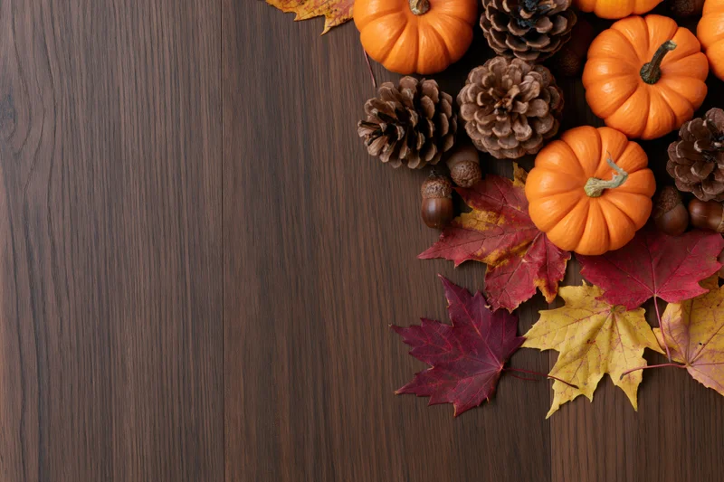 Small orange pumpkins, pinecones, acorns and maple leaves arranged in corner on dark wood surface