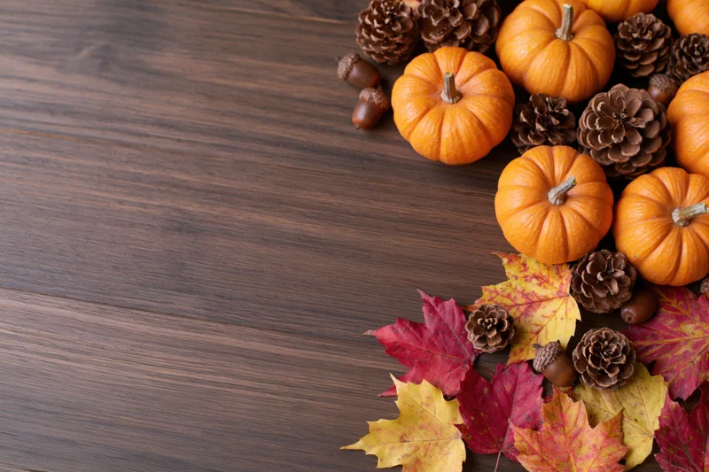 Small orange pumpkins, pinecones, acorns and autumn leaves arranged on a dark wooden table in a flat lay composition with copyspace