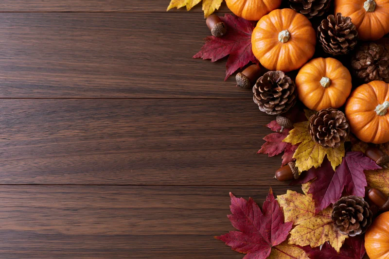 Small orange pumpkins, pinecones, acorns and autumn leaves arranged in corner on dark wooden table
