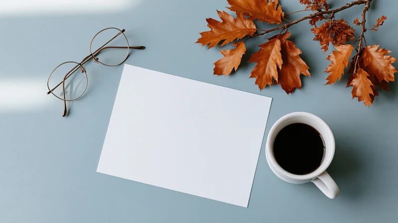 Blank white card with autumn leaves, coffee cup and glasses on blue surface