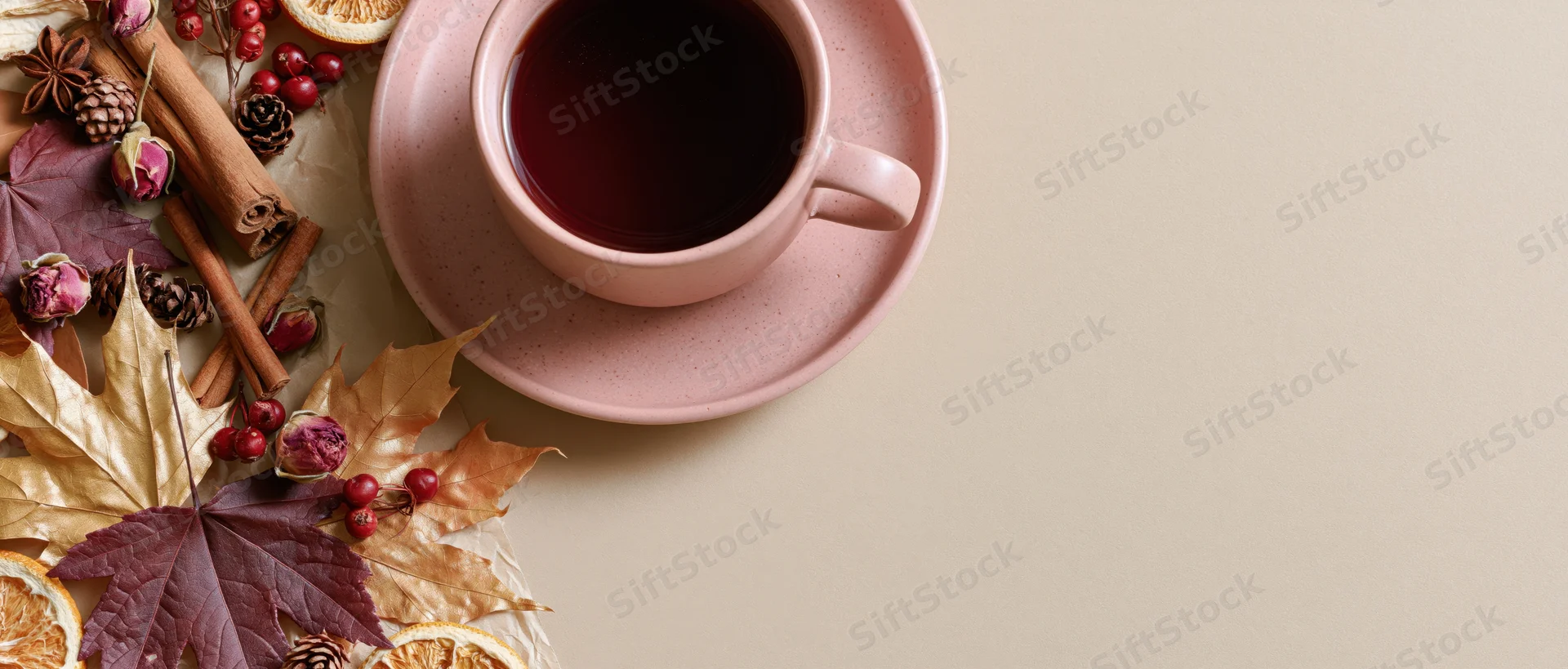 Pink ceramic cup of dark tea on saucer with autumn leaves, cinnamon sticks, pinecones and dried berries arranged on table surface
