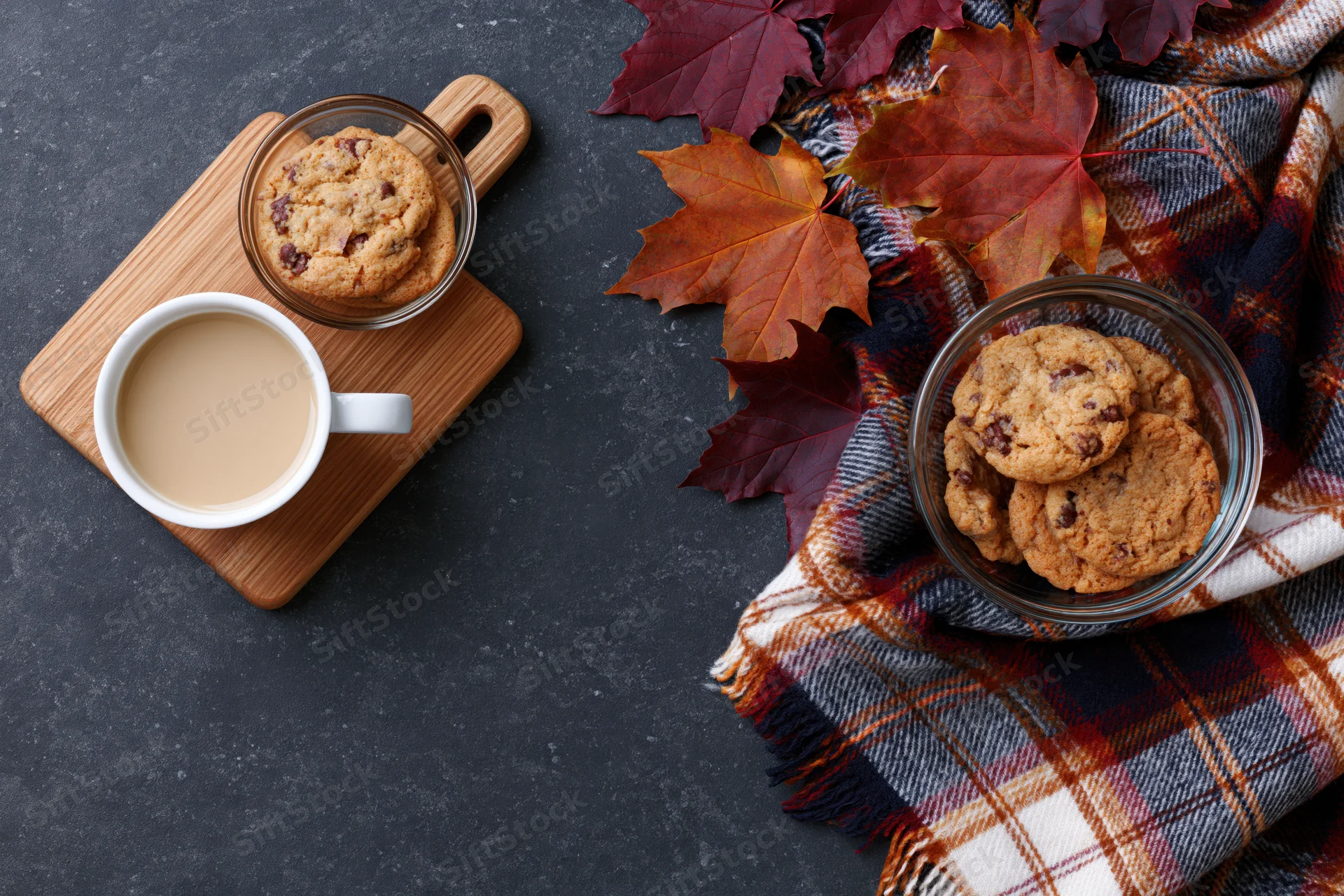 Overhead flat lay of a white mug of coffee with cookies on a wooden tray and autumn leaves on a plaid scarf