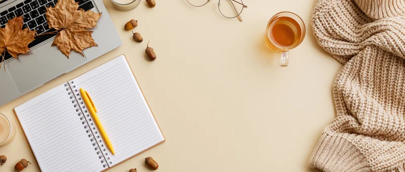 Autumn workspace flat lay with laptop, notebook, tea, sweater and acorns on beige surface