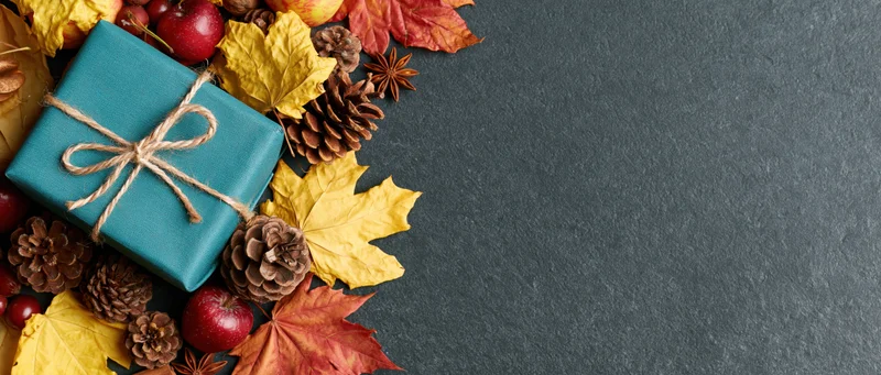 Autumn arrangement with gift box, pinecones, leaves and apples on dark surface