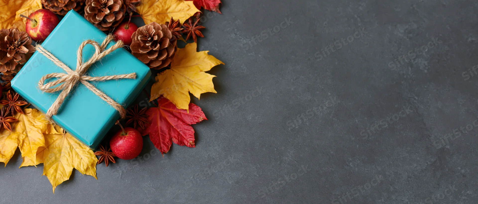 Autumn arrangement with gift box, leaves, pinecones and apples on dark surface