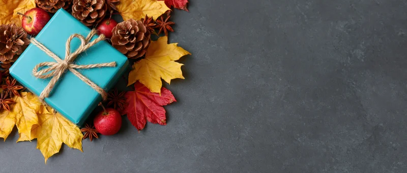 Autumn arrangement with gift box, leaves, pinecones and apples on dark surface