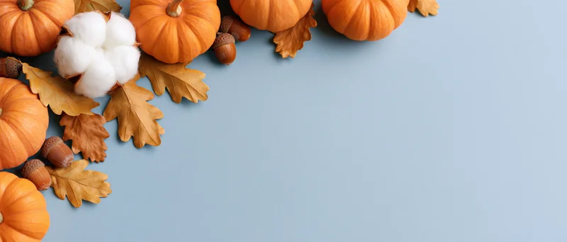 Small orange pumpkins and dried autumn leaves arranged in corner on blue surface with copyspace