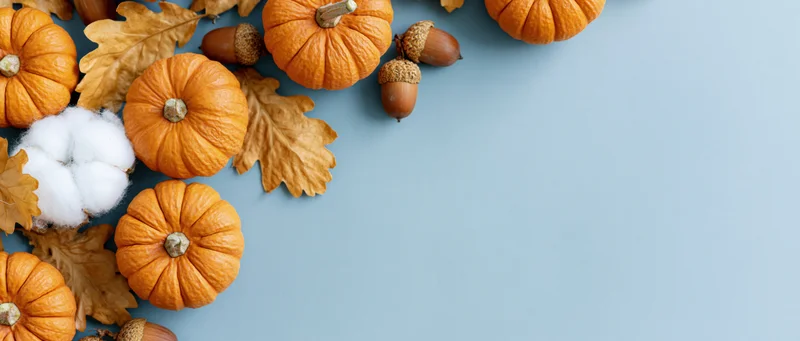 Small orange pumpkins and dried autumn leaves arranged on a blue surface with copyspace
