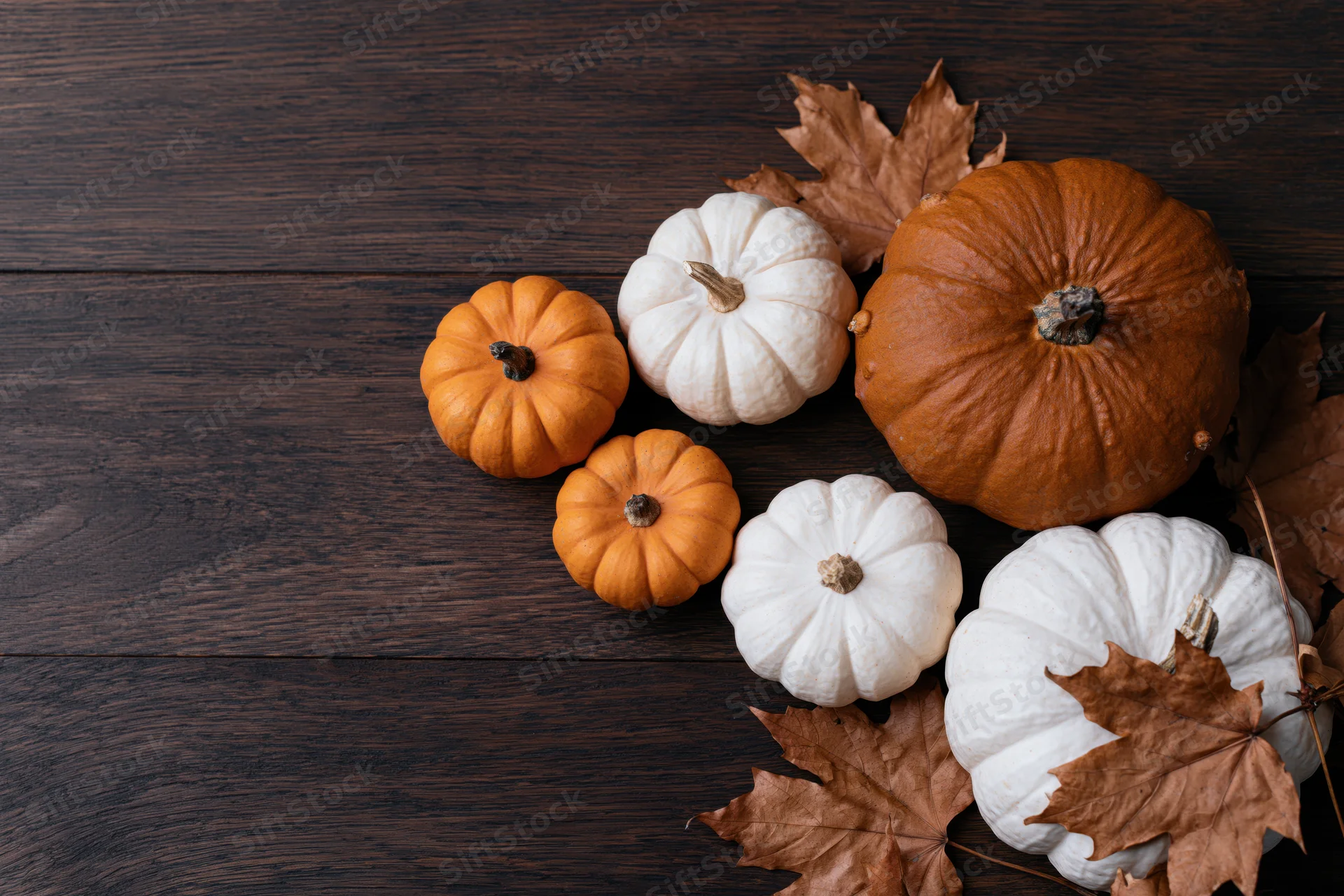 Pumpkins and autumn leaves arranged in bottom right corner on dark wooden table