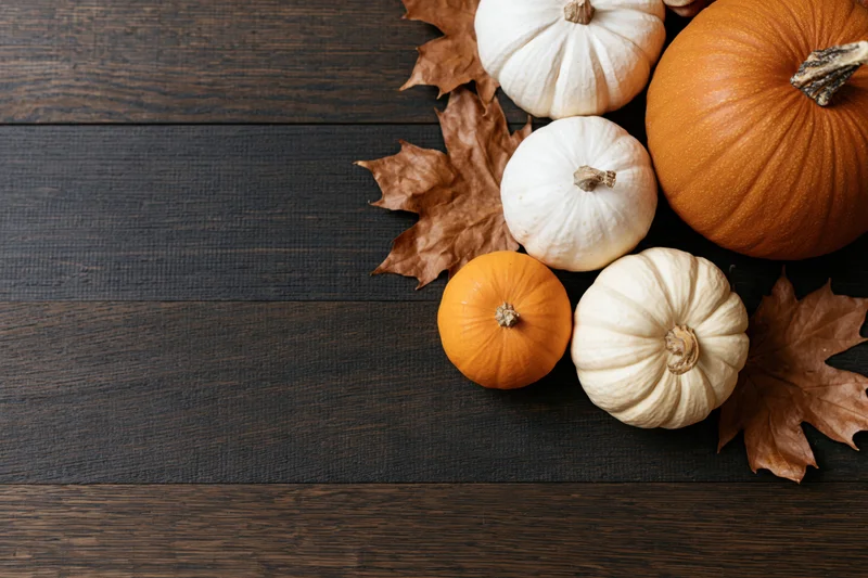 Pumpkins and dried maple leaves arranged in bottom-right corner on dark wooden table