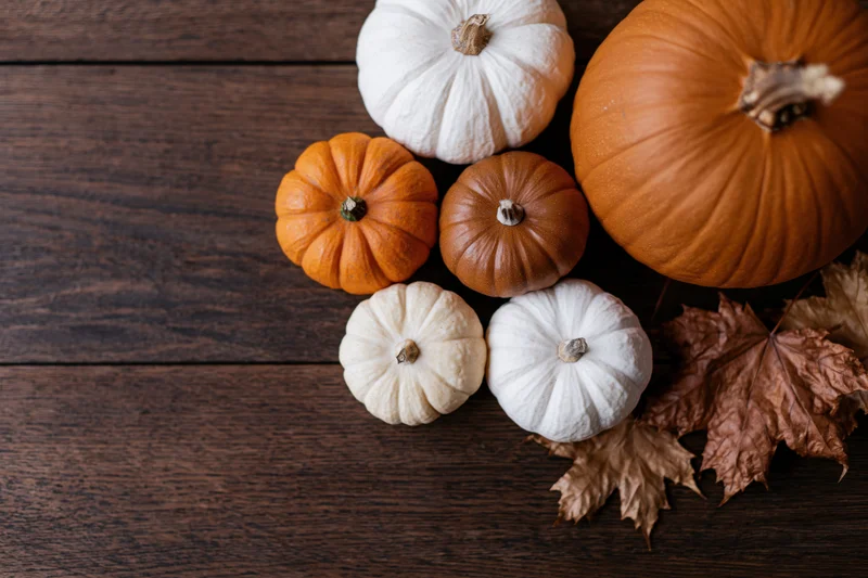 Pumpkins and dried maple leaves arranged in bottom right corner on dark wooden table