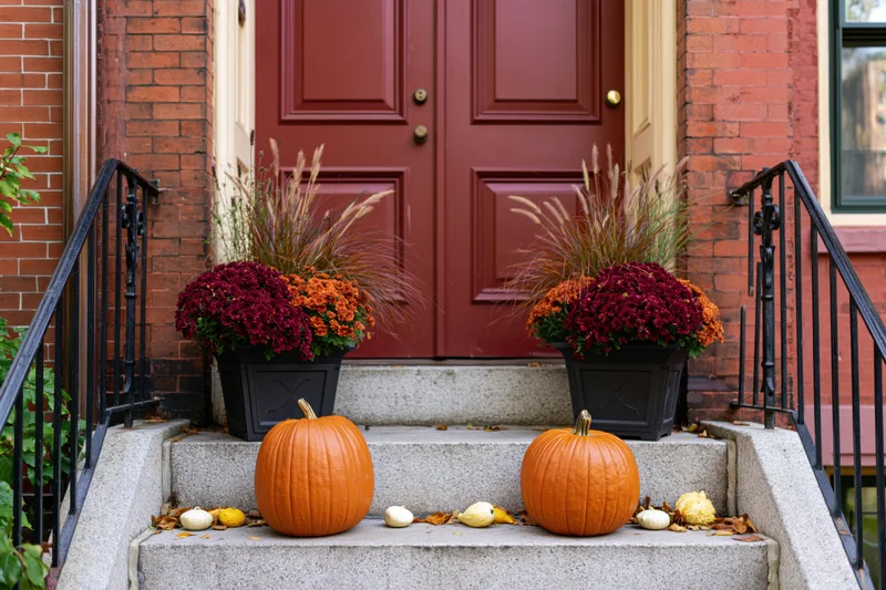 Autumn-decorated front stoop of a brick townhouse with pumpkins and potted flowers on stone steps