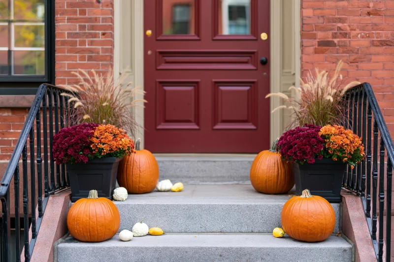 Pumpkins and potted mums arranged on front stoop steps of brick townhouse with red door