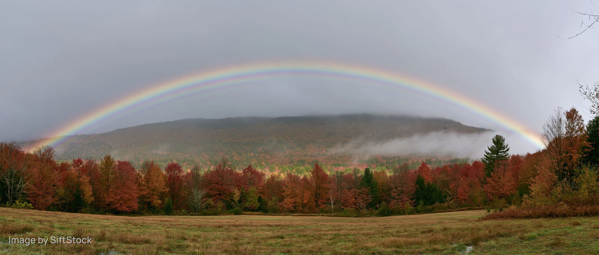 Double rainbow arching over autumn forest with misty mountains and colorful foliage in a rural meadow