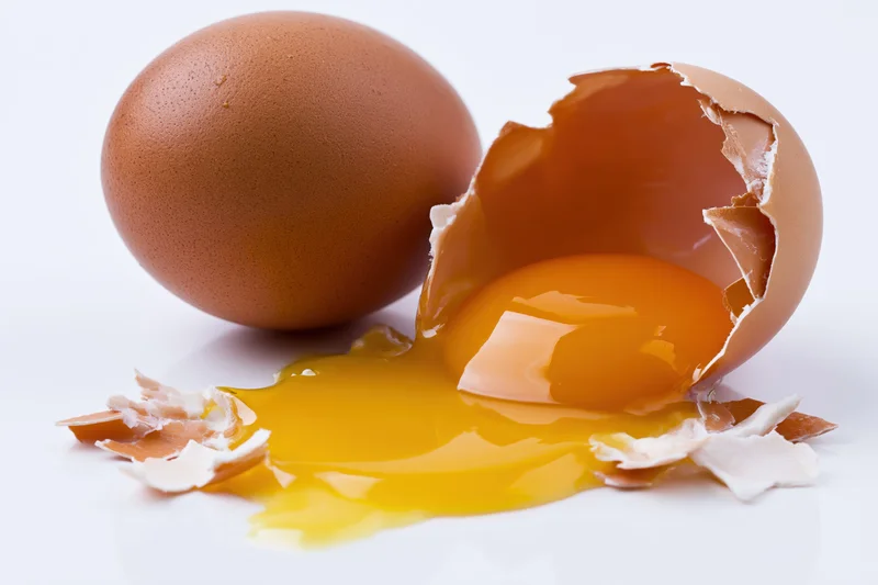 Cracked brown chicken egg split open on flat white surface with yolk spilling out