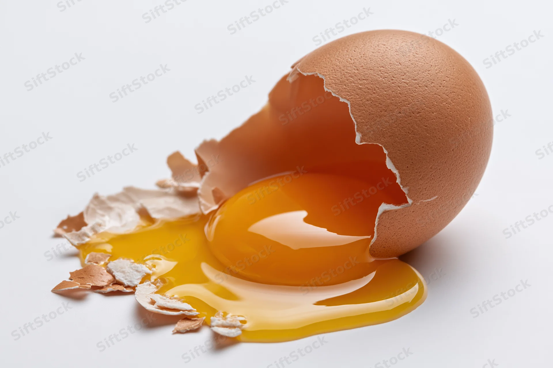 Cracked brown chicken egg with yolk spilling onto flat white surface