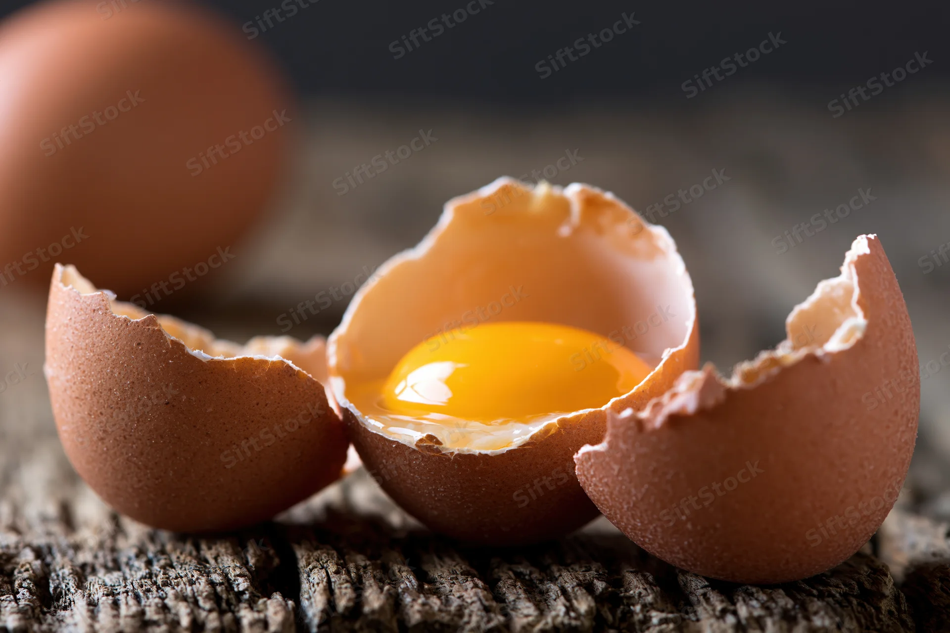 Cracked brown chicken egg split open revealing bright orange yolk on wooden surface