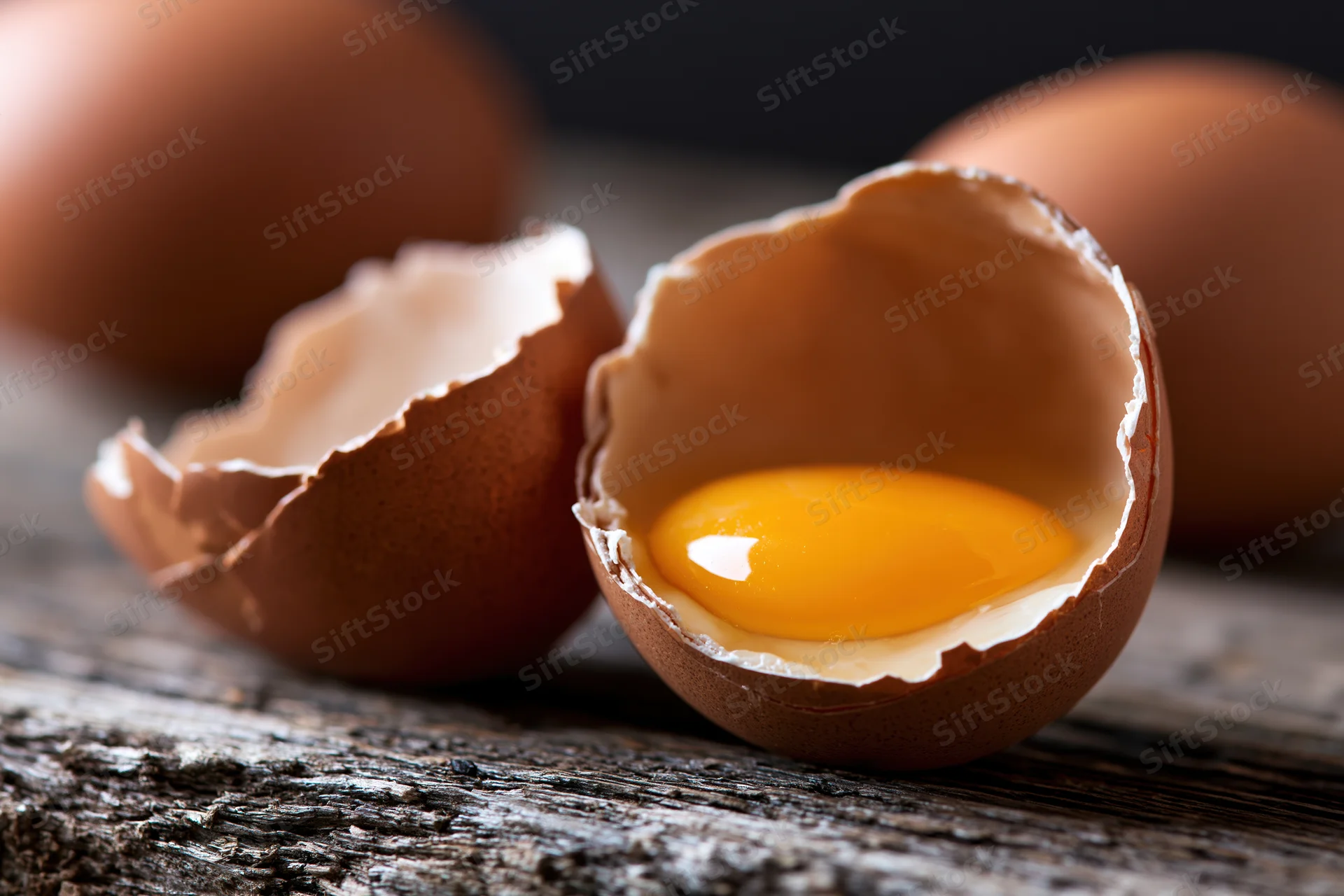 Cracked brown chicken egg split open revealing bright orange yolk on wooden surface
