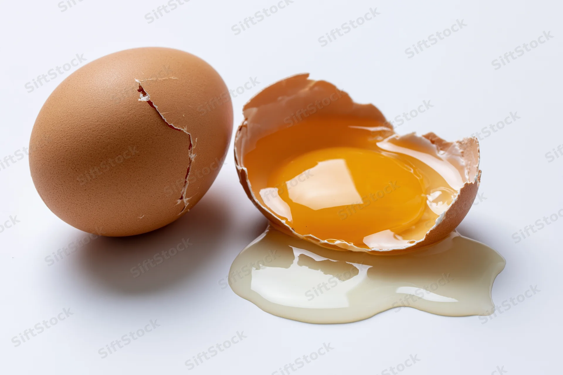 Cracked brown egg broken open on white surface with yolk and white spilled out