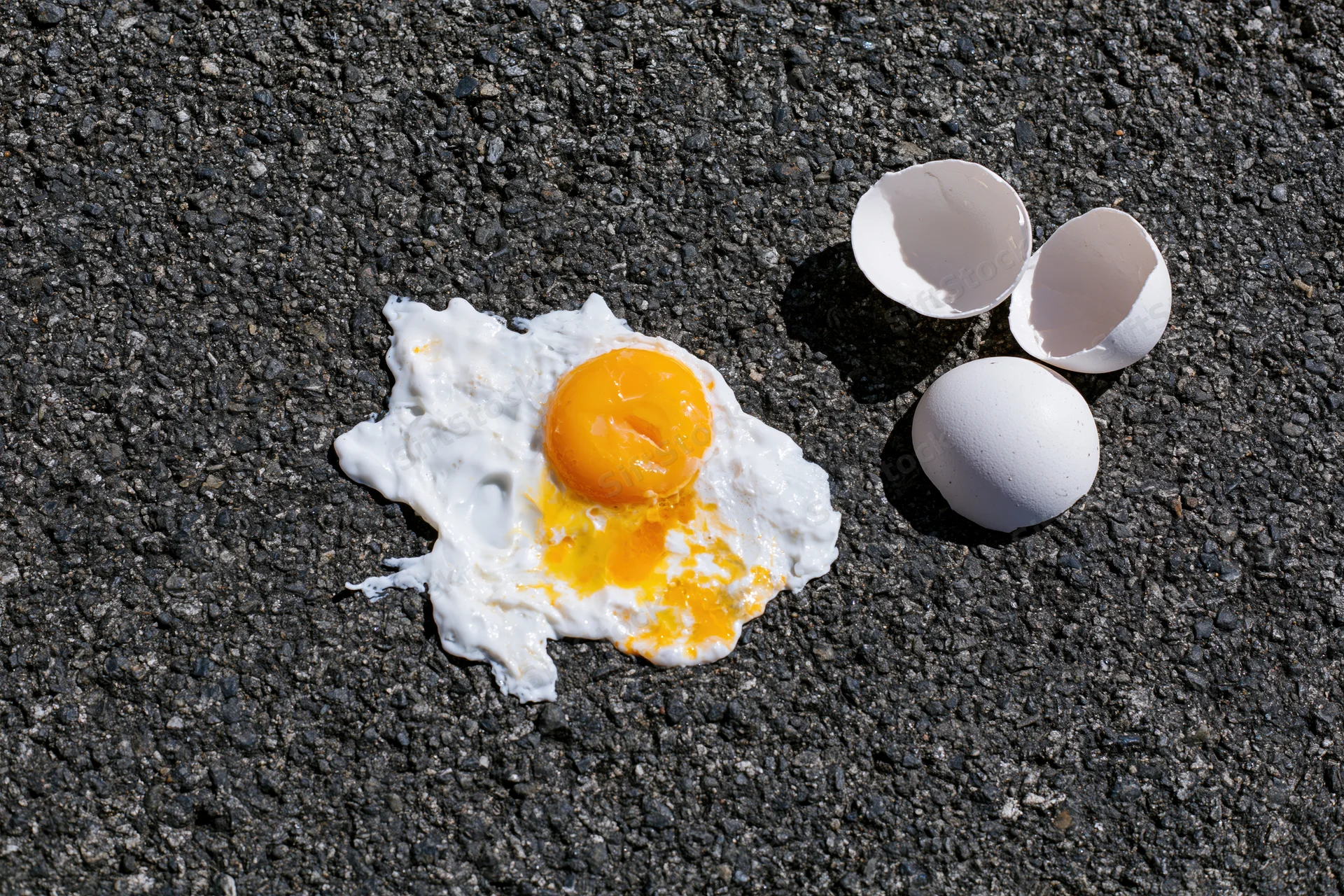Fried egg on hot dark asphalt pavement with cracked shell and yolk visible