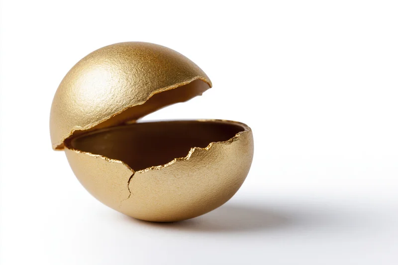 Cracked golden egg split into two halves with top shell lifted on white background