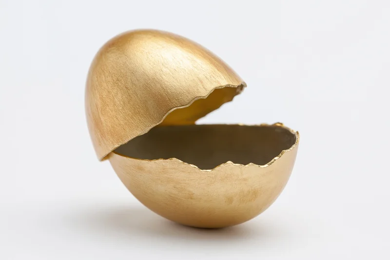 Golden egg split open with top half lifted on white background