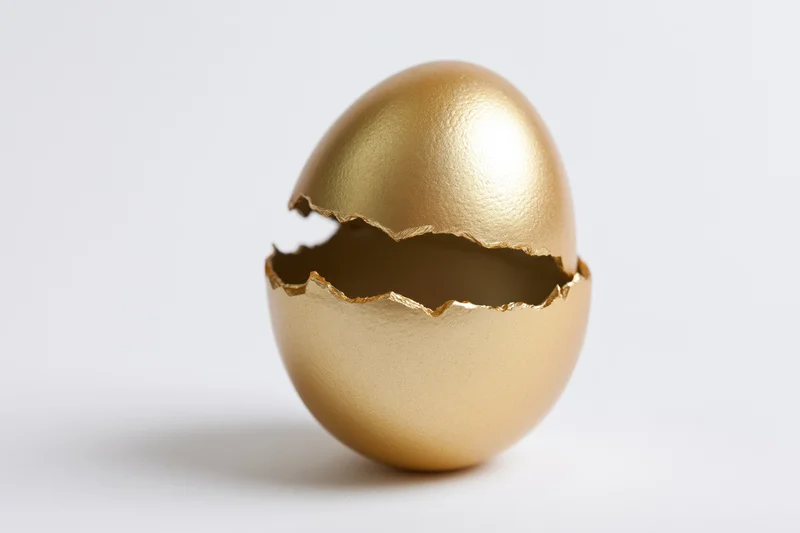 Golden egg split open with top half lifted on white background