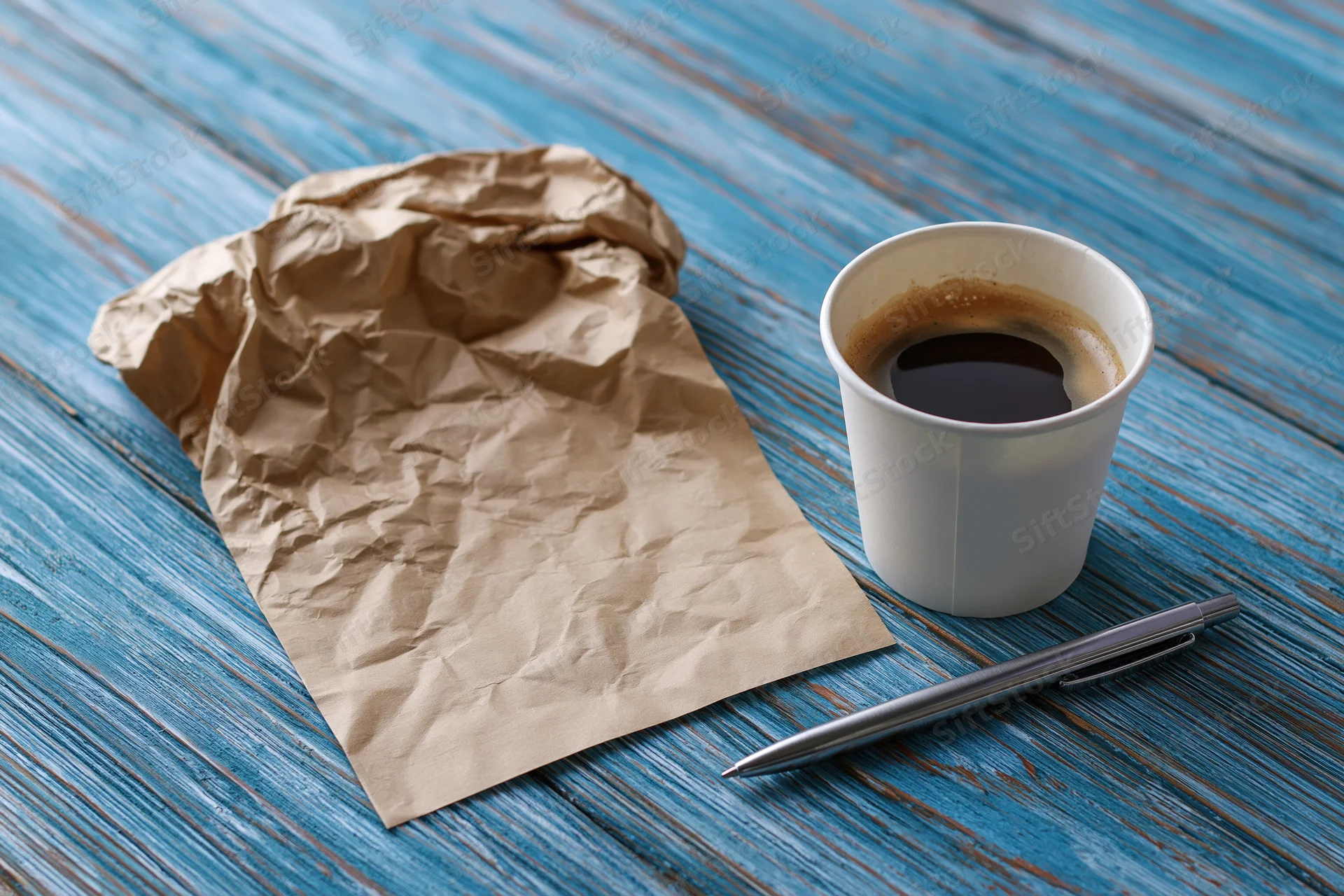 Crumpled kraft paper note beside a coffee cup and pen on a blue wooden table