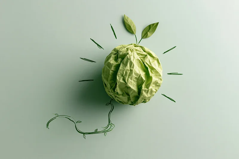 Crumpled green paper ball styled as a lightbulb with hand-drawn leaves and vine on a plain background