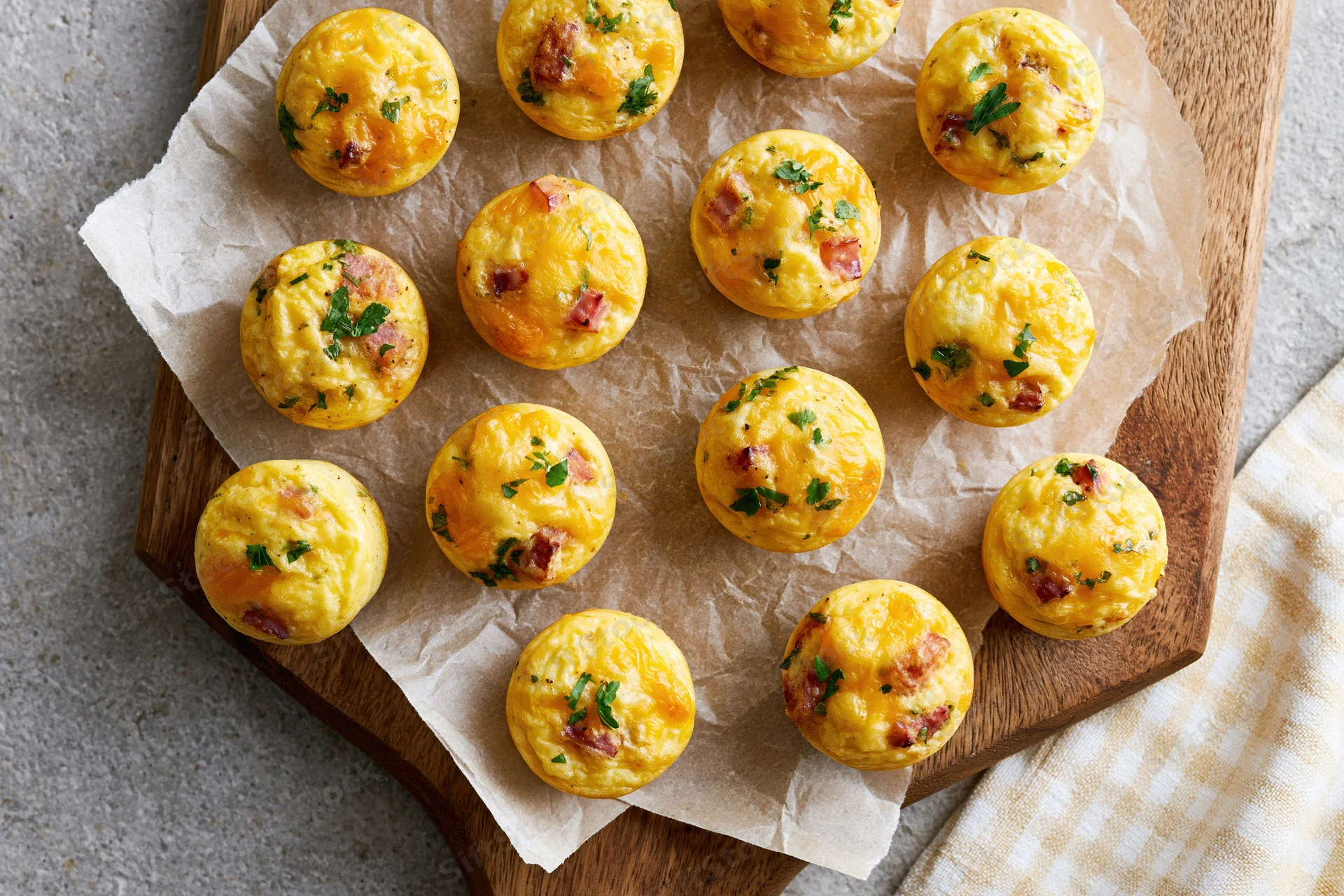 Small baked egg muffins with ham and cheese arranged on parchment paper on a wooden board