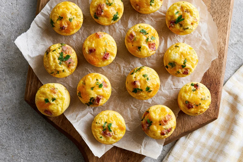 Small baked egg muffins with ham and cheese arranged on parchment paper on a wooden board