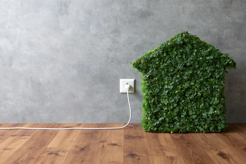 House-shaped clover topiary plugged into wall socket on wooden floor against concrete wall