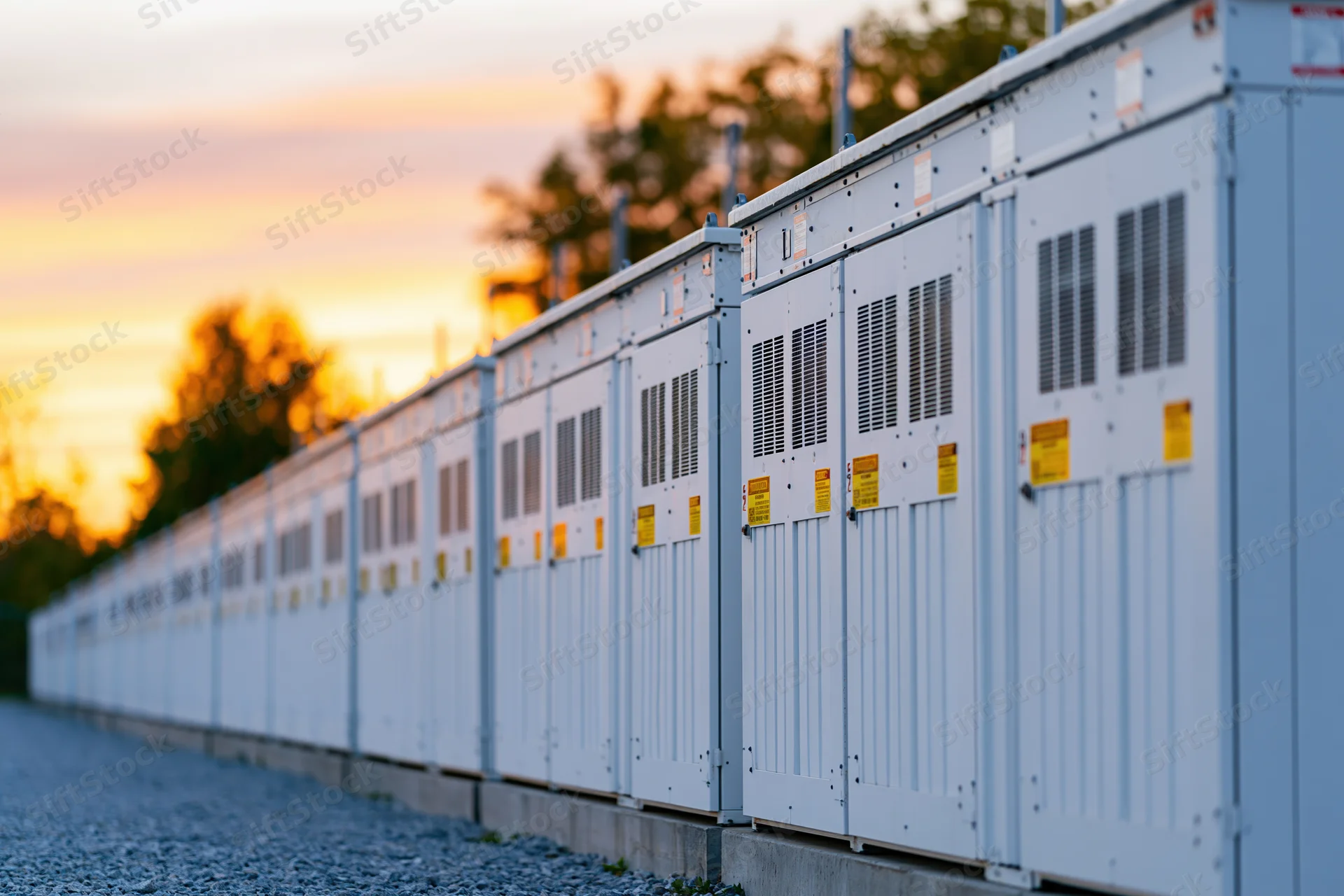 Row of white industrial battery energy storage containers outdoors at sunset