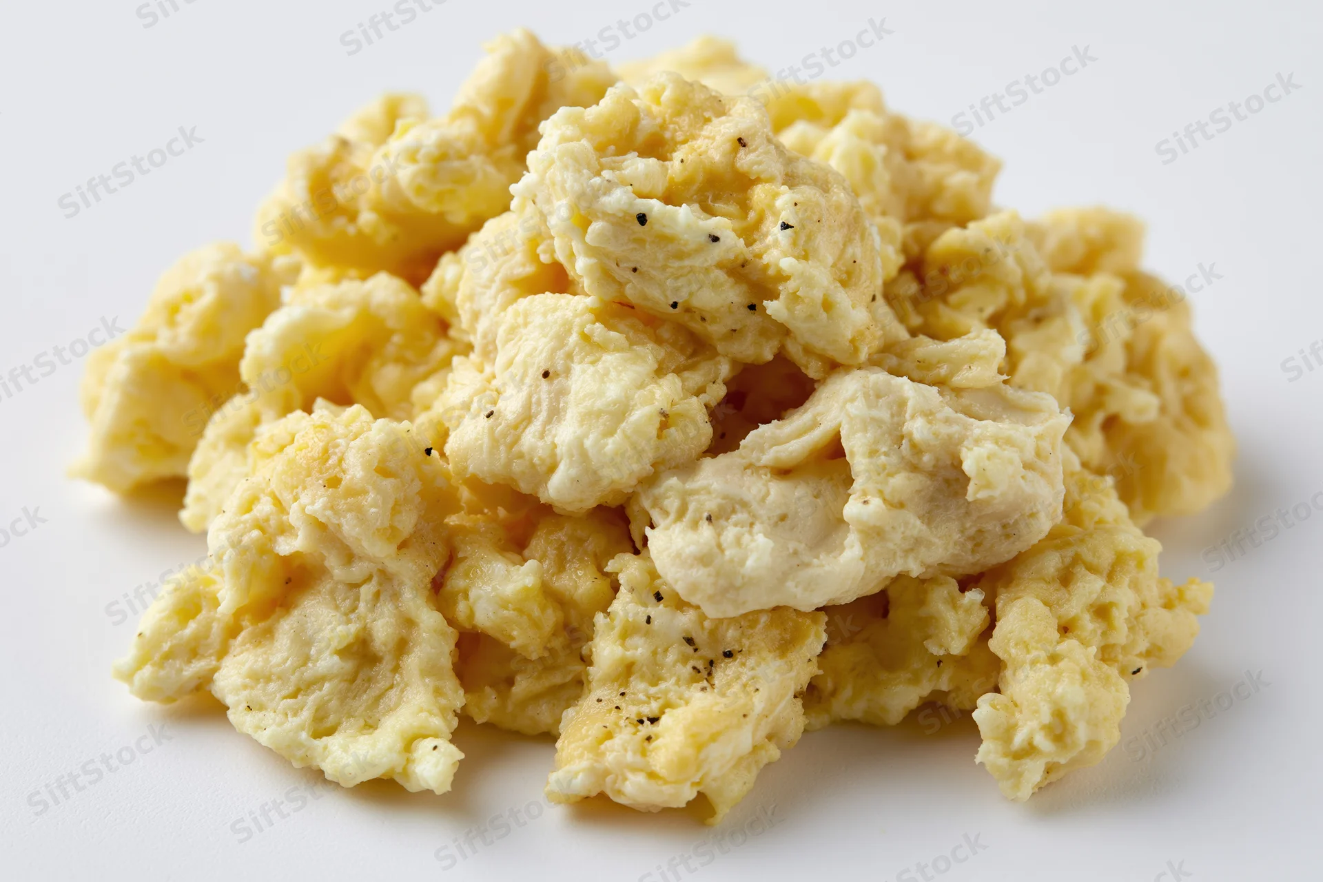 Pile of scrambled eggs with black pepper on plain white surface
