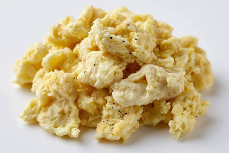 Pile of scrambled eggs with black pepper on plain white surface