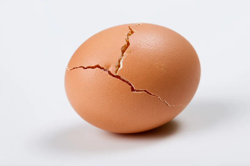 A single brown chicken egg with a jagged crack across its shell, isolated on white