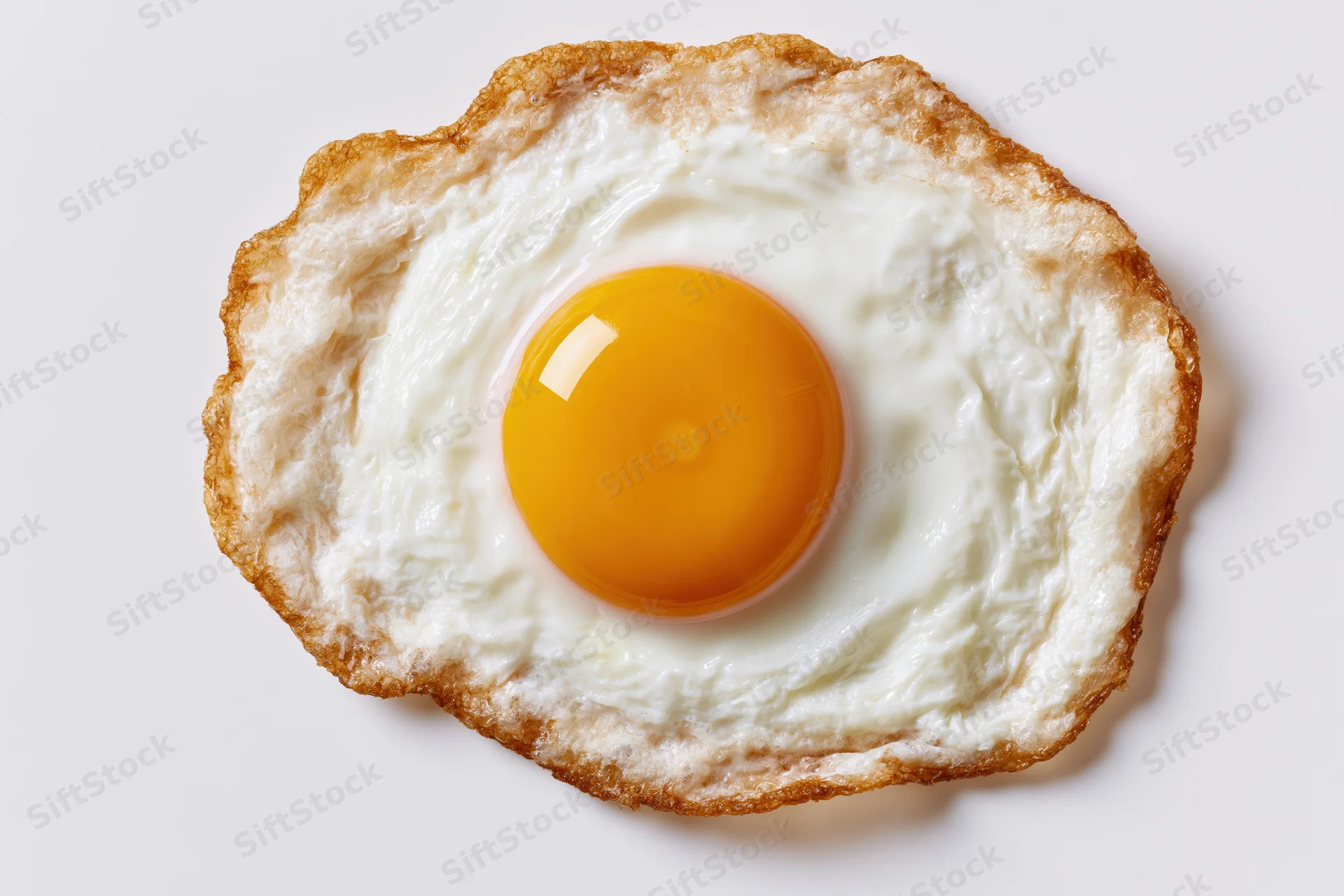 Single fried egg viewed from directly above on a plain white surface